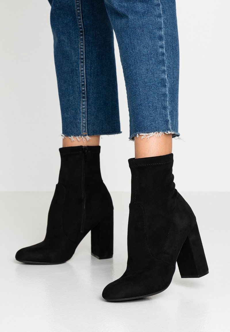 Schwarze Wildleder-Ankle-Boots mit spitzem Zehenbereich und Blockabsatz. Das Design zeichnet sich durch eine glatte Textur und einen seitlichen Reißverschluss für ein einfaches An- und Ausziehen aus.