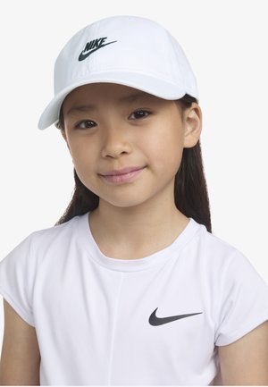 Hvid Nike baseballkasket med grønt logo, båret sammen med en hvid Nike t-shirt med en sort swoosh. Glat stof, struktureret form.