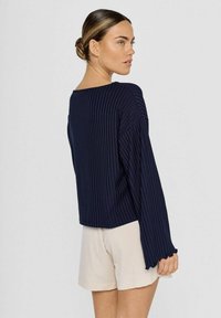 Marineblauw geribbelde lange mouwen top met een bootvormige halslijn en uitlopende mouwen, gecombineerd met lichtbeige shorts. Matte textuur, casual ontwerp.