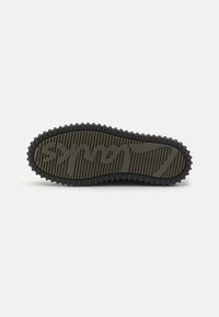 Sole boty s hlubokým vzorem a vystouplým textovým logem "Clarks" v písmu, zobrazené ploché na bílém pozadí.