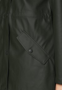 Tmavě zelená nepromokavá bunda s hladkým povrchem, vybavená velkou šikmou klopovou kapsou uzavíranou černým patentkem.