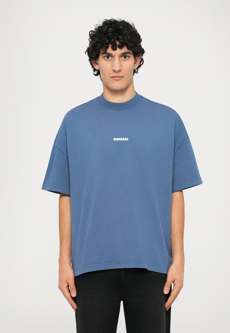 Blue cotton t-shirt with a high neckline and short sleeves. Features white "BONSAI" text on the chest, loose fit, and straight hem.