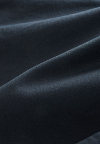 Mørk marineblåt tekstil med en glat, let struktureret overflade. Stoffet er arrangeret i bløde folder, der fremhæver dets fald og dybde.