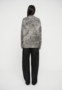 Sweatshirt cinza, texturizado, de manga longa com um padrão abstrato subtil, combinado com calças largas pretas de perna larga, visto por trás.