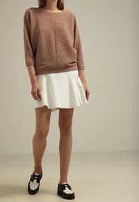 Suéter marrón texturizado con mangas de 3/4, combinado con una falda blanca acampanada y zapatos bicolor en blanco y negro con hebillas.