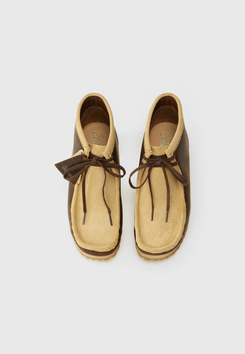 Chaussures en daim beige et marron avec une forme arrondie, dotées d'une coupe basse, de lacets en cuir et de semelles en caoutchouc. Remarquables par leurs couleurs contrastées et leurs détails texturés.