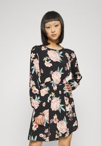 Vestido floral preto com mangas longas e cinto na cintura. Apresenta rosas cor-de-rosa e folhas verdes. Tecido suave, corte até ao joelho e ajuste descontraído.