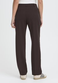 Pantalon marron ajusté avec une coupe droite, présentant une texture lisse, deux poches arrière et une taille mi-haute.
