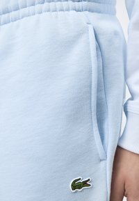 Pantalon de jogging bleu clair avec taille élastique et poche latérale, avec un petit logo crocodile vert près de la poche.