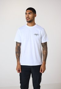 Weißes Baumwoll-T-Shirt mit kurzen Ärmeln und Rundhalsausschnitt, mit schwarzem Druckgrafik auf der linken Brust. Glatte Textur, normale Passform.