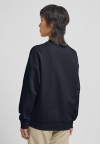 Felpa navy con polsini e orlo a coste, colletto rotondo e spalle scese, che presenta una texture morbida e una vestibilità rilassata.