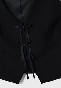 Black vest featuring a deep V-neck, satin lining, and two ribbon-tied closures at the front. Smooth texture with a tailored cut.