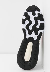 Semelle d'une basket avec des pods en caoutchouc noirs et blancs pour la traction et une surface texturée, sur un fond clair.