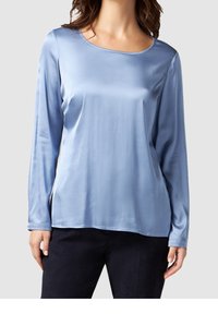 Light blue long-sleeve blouse made of satin with a round neckline and a smooth texture. Features a relaxed fit and side slits.