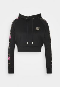 Sweat à capuche court noir avec cordons, logo doré sur la poitrine et chaîne décorative dorée avec motif de pierre précieuse rose le long des manches.