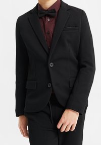 Svart texturerad blazer med notch-lapels, två knappar och sidofickor, bärs över en vinröd mönstrad skjorta och svart fluga.
