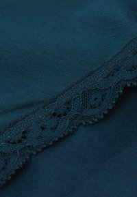 Marinblått stickat tyg med delikat svart spetskant som har vågiga kanter och ett blommönster längs fållen. Slät textur, minimal glans.