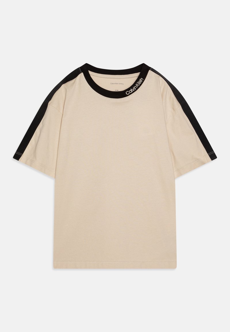 T-shirt de algodão bege com mangas curtas, apresentando detalhes pretos nos ombros e uma etiqueta preta na gola com o texto "Calvin Klein".