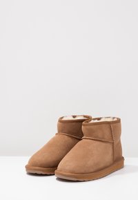 Stivali ankle in suede marrone con una morbida fodera, design a taglio basso e suola in gomma; presenta cuciture decorative lungo il bordo.