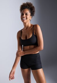 Svart, ribbestrikket sports-bh og matchende høyhåndte shorts; sømløst, stretchy materiale med en jevn tekstur, egnet for aktiv bruk.