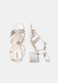 Sandali con tacco a stiletto argentati e con cinturini, dal finish lucido, dotati di un tacco basso a blocco, cinturino alla caviglia regolabile e decorazioni decorative.