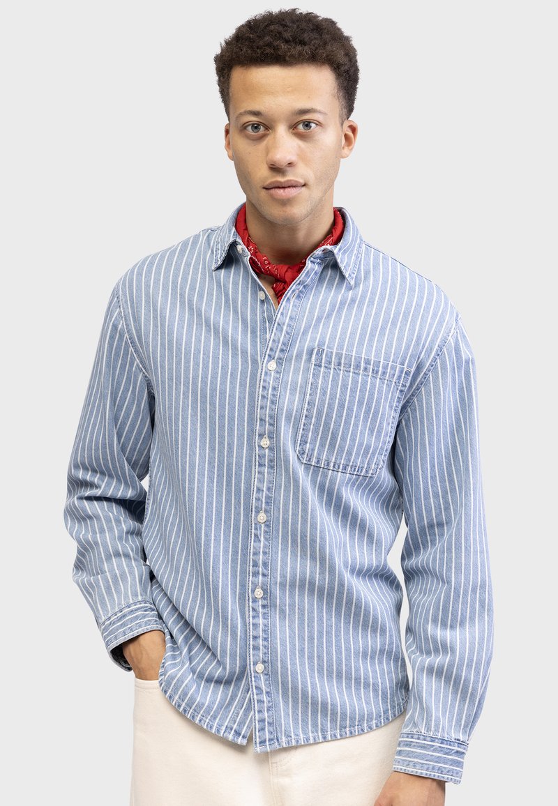 Light blue button-up shirt featuring vertical white stripes, a left breast pocket, and a soft cotton texture, paired with a red bandana.