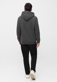 Grijze hoodie met een trekkoordcapuchon, ribbelmanchetten en -zoom, gecombineerd met zwarte broek en crèmekleurige sneakers, gezien van achteren.