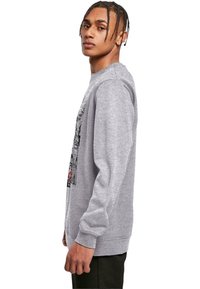 Šedá mikina s dlhými rukávmi, rebrovanými manžetami a grafickým dizajnom. Mäkká textúra a uvoľnený strih, s čiernymi a červenými akcentmi.