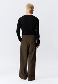 Top negro de manga larga combinado con pantalones anchos a rayas marrones de cintura alta, con bolsillos traseros y tela texturizada.