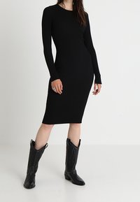 Abito midi nero a costine con maniche lunghe, forma aderente e scollatura tonda. Abbinato a stivali cowboy neri con cuciture decorative.