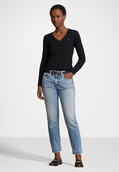 Pulover negru din tricot cu model texturat, cu decolteu în V, asortat cu blugi drepti ușor deteriorați, de culoare albastru deschis, și mocasini negri. Lipsă detaliu curea.