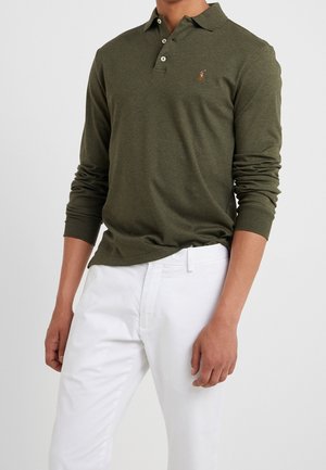 Koszulka polo z długim rękawem w kolorze oliwkowej zieleni, wykonana z bawełny, z plisą na dwa guziki i wyhaftowanym logo. Połączona z białymi spodniami.