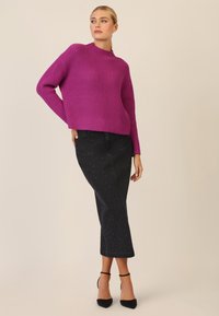 Maglione a coste viola con collo alto, abbinato a una gonna di jeans nera con piccole decorazioni e scarpe con tacco nere.