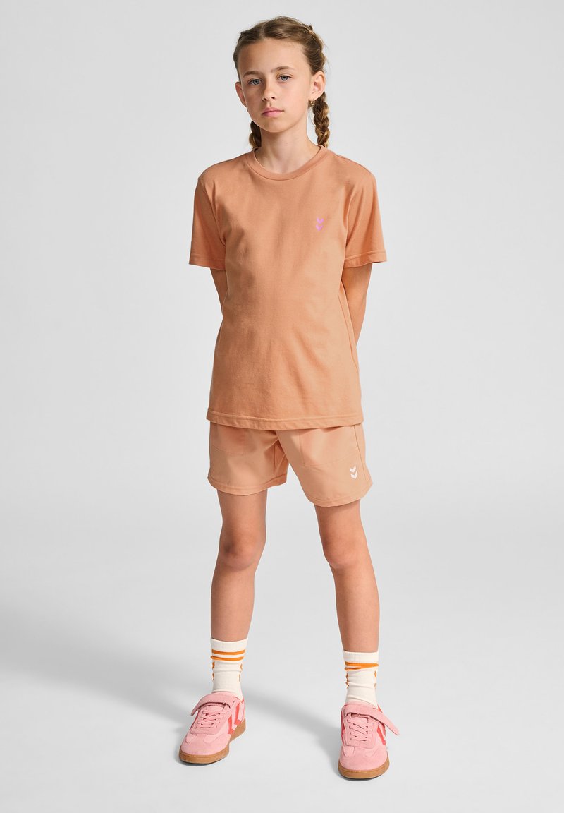 Sæt bestående af ferskenfarvet bomulds t-shirt og shorts, med et lille pink logo. Tilbehøret inkluderer pink sko og stribede sokker med orange detaljer.