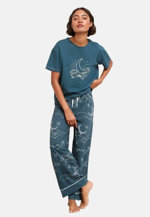 Türkisfarbenes Baumwoll-Pyjama-Set mit Mond- und Wolkenmotiv. T-Shirt mit Frontgrafik, während die weit geschnittenen Hosen einen Kordelzugbund und einen kontrastierenden Besatz haben.