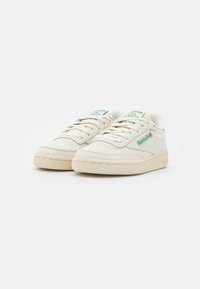Pair of off-white Reebok leather sneakers with green logo, laces, and beige rubber soles on a white background.