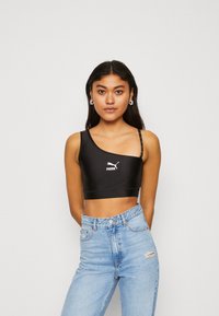 Top corto nero con una spallina, realizzato in tessuto liscio. Presenta il logo PUMA in bianco, abbinato a jeans a vita alta di colore azzurro chiaro.