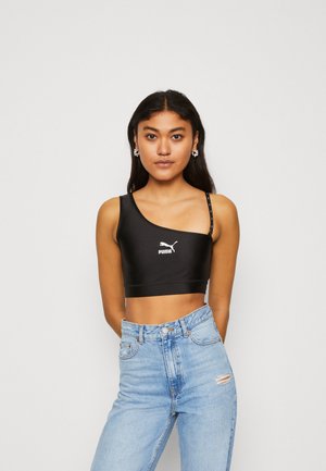 Svart crop top med én skulderstropp, laget av glatt stoff. Har PUMA-logo i hvitt, stylet med lyseblå høy i livet jeans.