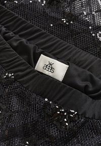 Tissu noir paillette avec un design en maille texturée et une ceinture en satin lisse avec une étiquette blanche. L'apparence générale est brillante.