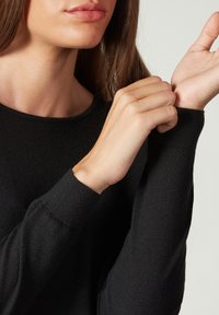 Czarny dzianinowy sweter z okrągłym dekoltem; zbliżenie na rękę regulującą mankiet, ukazujące miękką teksturę i dopasowane rękawy.