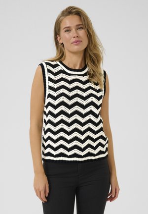 Top en tricot sans manches avec un motif en zigzag noir et blanc. Présente un col et un ourlet côtelés. Le tissu semble texturé et respirant.