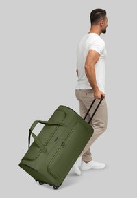 Olivgrüner Duffle Bag mit zwei schwarzen Rollen, stabilen Griffen und einem Reißverschlussfach. Das Material wirkt strapazierfähig und strukturiert.