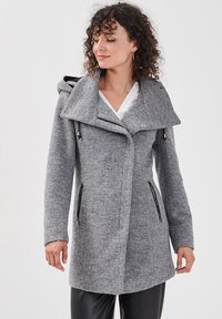 Manteau en mélange de laine gris avec capuche, col asymétrique, poches zippées à l'avant et finition texturée. Manches longues et silhouette cintrée.