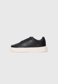 Fekete bőr sneaker, lekerekített orral, fűzős elejével és domború logóval. Vastag fehér talppal rendelkezik, ami kontrasztot ad.