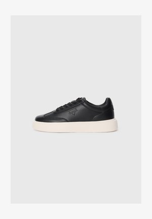Svart lær-sneaker med rund tå, snøring foran og preget logo. Har en tykk hvit såle for kontrast.