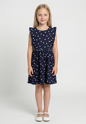 Abito blu navy con pois bianchi, spalline arricciate e vita elastica. Abbinato a scarpe basse bianche.