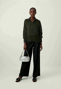 Σκούρο πράσινο πουκάμισο με υφή, συνδυασμένο με φαρδύ μαύρο παντελόνι. Αξεσουάρ με ασημένια τσάντα και μαύρα σανδάλια.