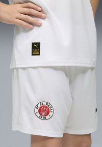 Vitt fotbollskit bestående av en t-shirt med korta ärmar och shorts. T-shirten har en svart Puma-logga och shortsen visar en cirkulär FC St. Pauli-märke.