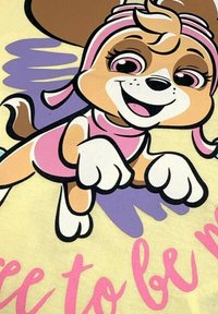 Un personnage de chien en dessin animé avec du pelage brun, portant une tenue rose et un bandeau, entouré de graphiques violets et jaunes ; le texte indique "Libre d'être moi."