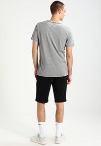 T-shirt gris à rayures, à manches courtes, assortie à un short noir. Des chaussettes blanches jusqu'aux genoux et des baskets légères complètent le look décontracté.